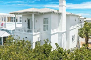 A white two-story building with a balcony, a chimney, and a porch.