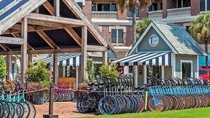 A hotel with a covered outdoor seating area, a bike rental station, and a small building with a clock.