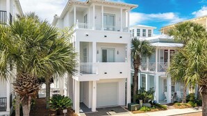 A two-story white building with a garage, surrounded by palm trees.