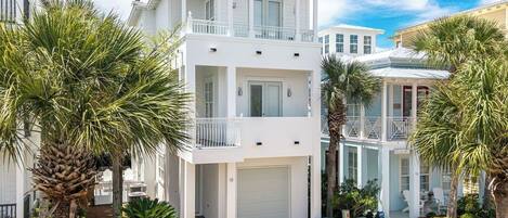 A two-story white building with a garage, surrounded by palm trees.