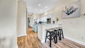 A modern kitchen with a central island, bar stools, and a painting on the wall.