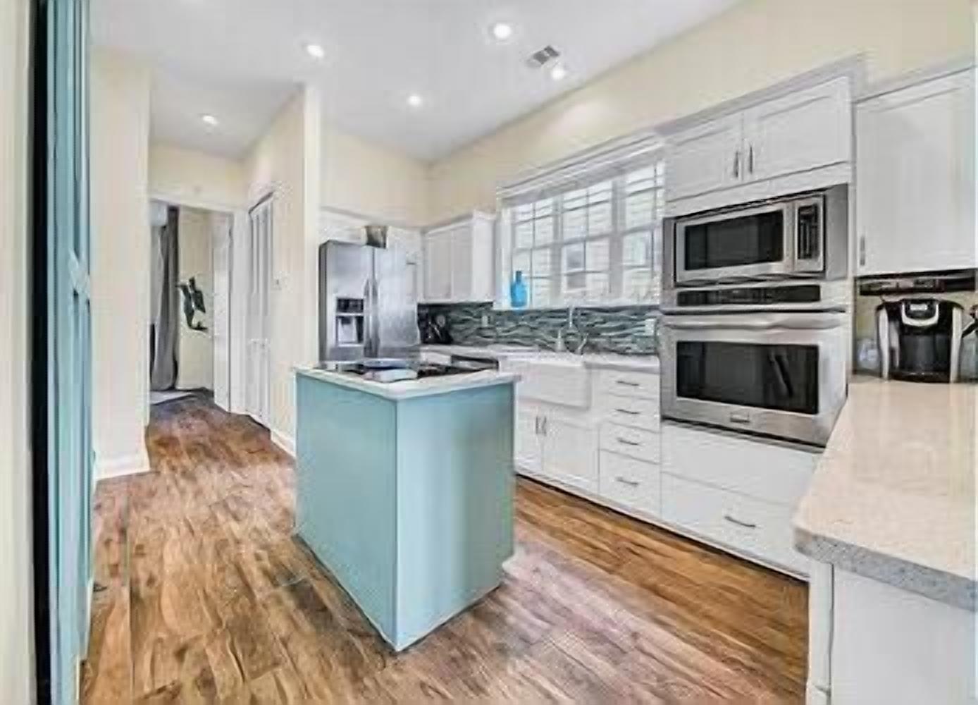 A modern kitchen with white cabinets, a central island, stainless steel appliances, and a wooden floor.