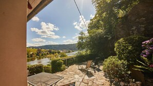 Un patio con suelo de piedra, una mesa y sillas, con vistas a un río y colinas.