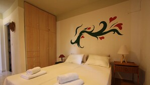 A hotel room with a large bed, two bedside tables, a wooden wardrobe, and a wall mural. - Mandola Studios - Garden view Studio (Kefalonia)
