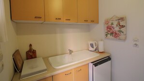 A kitchen with a white sink, wooden cabinets, and a small refrigerator. - Mandola Studios - Garden view Studio (Kefalonia)