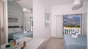 Een moderne slaapkamer met balkon, een bed met blauw beddegoed, een nachtkastje met toiletartikelen en een groot raam met uitzicht op de bergen.
