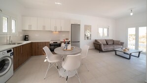 Een moderne keuken met witte kasten, een ingebouwde wasmachine en een eethoek met een ronde tafel en witte stoelen.