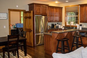 A modern kitchen with wooden cabinets, a stainless steel refrigerator, a bar area, and a dining table with chairs. - Charming Cabin in Deep Creek (Swanton)