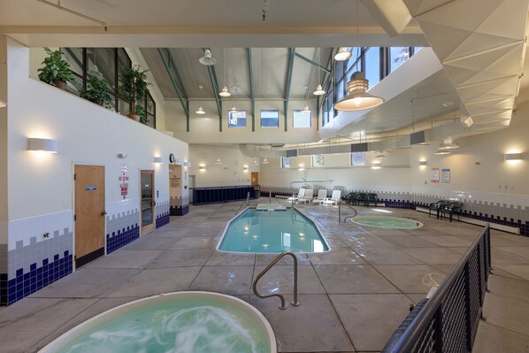 Un área de piscina interior con varias piscinas, un letrero que indica que no se permite bucear y un espacio de descanso con sillones.