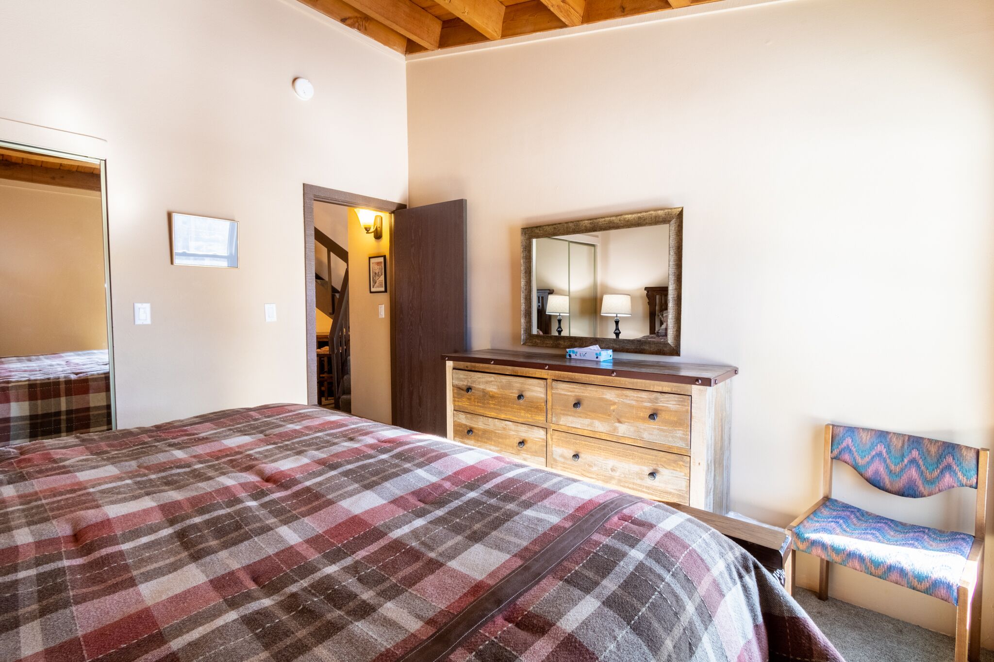 A bedroom with a large bed, a wooden dresser, a chair, and a mirror.