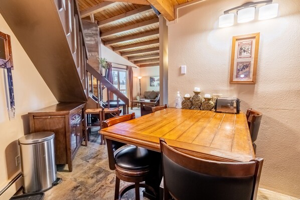 Un espace repas comprenant une grande table en bois, des chaises et un escalier menant à un niveau supérieur.