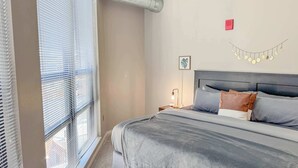 A bedroom with a bed, a nightstand, a wall-mounted light, and a window with blinds. - Apartment near Kerrytown Concert House (Ann Arbor)