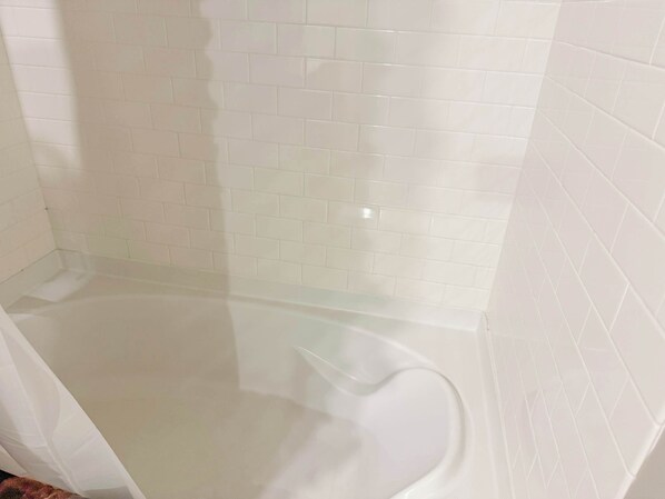 Un baño con paredes de azulejos blancos y una bañera de vidrio transparente.