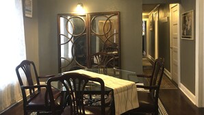 A dining area with a glass table, dark wooden chairs, a decorative metal partition, and a ceiling fan.