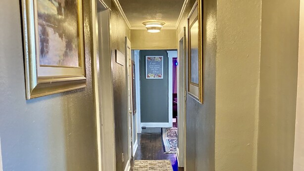 A hallway with framed artwork on the walls, a patterned rug on the floor, and a ceiling light.