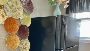 A black refrigerator in a kitchen with decorative plates on the wall and a vase with flowers.