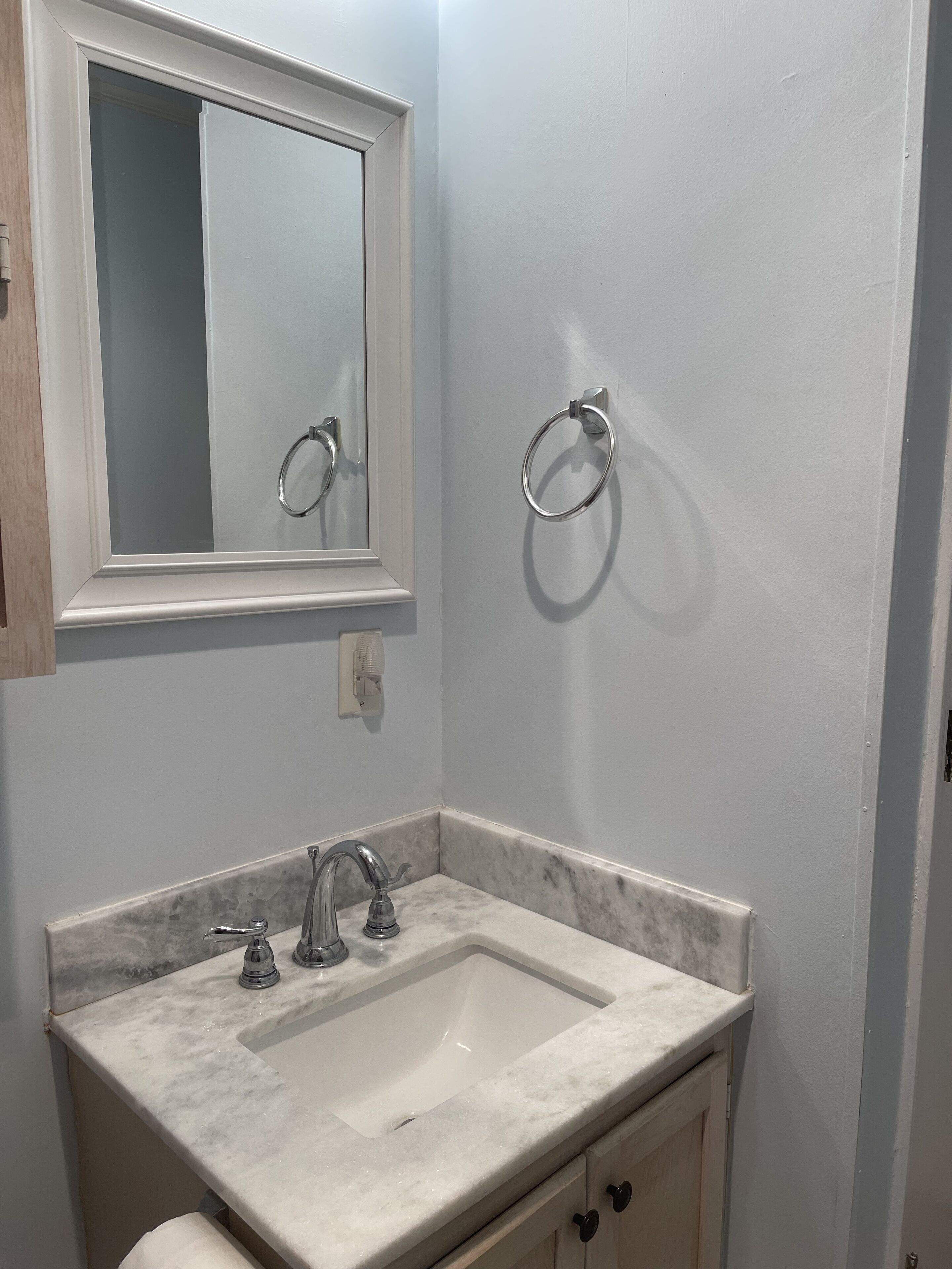 Une salle de bain avec un lavabo blanc, un miroir et deux porte-serviettes fixés au mur.