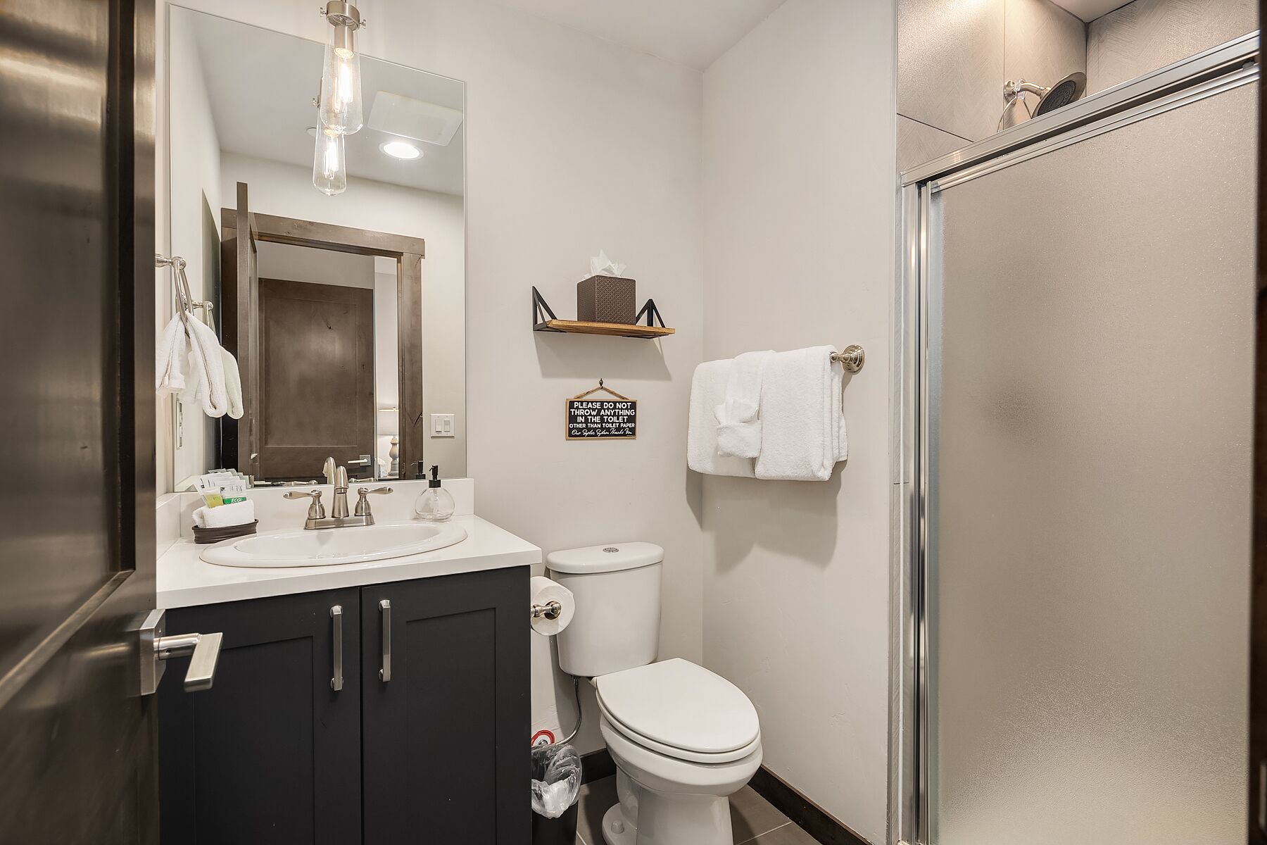 A modern bathroom with a sink, toilet, and shower. There is a sign on the wall and towels hanging on the wall.