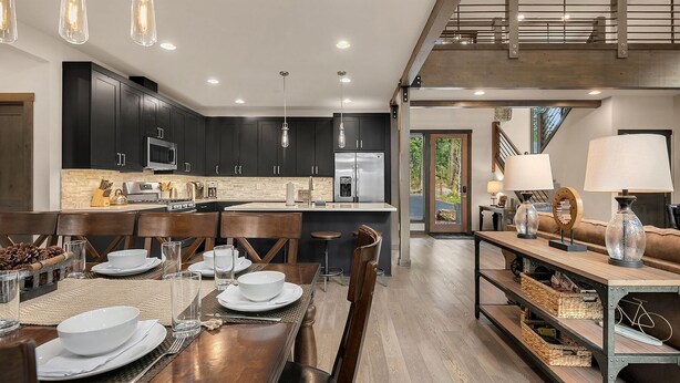 Una cocina moderna con armarios oscuros, una isla central y una zona de comedor con una mesa y sillas de madera.