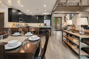 Een moderne keuken met donkere kastjes, een centraal eiland en een eethoek met een houten tafel en stoelen.
