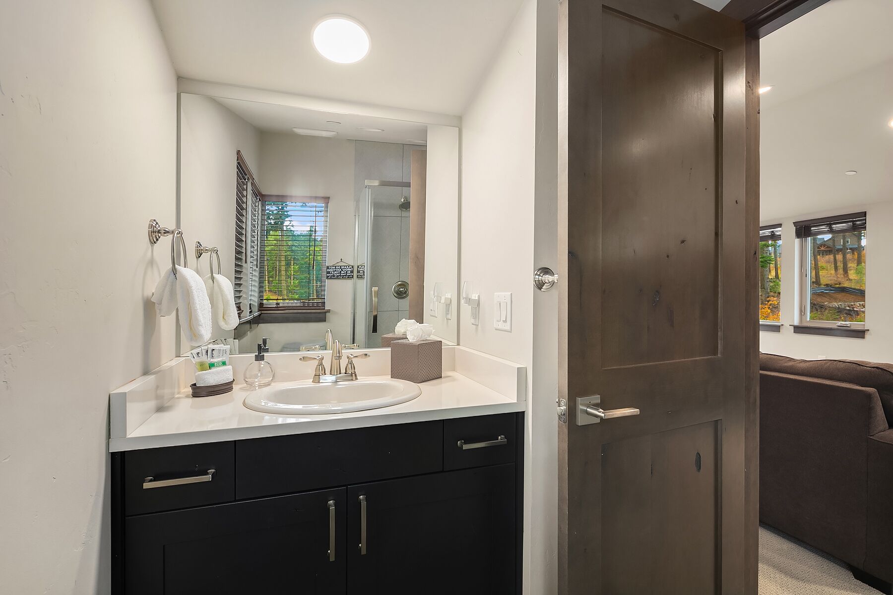 Un baño moderno con un espejo grande, lavamanos blanco y armarios oscuros.
