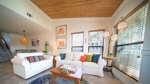 A living room with two white sofas, a coffee table, and a blue patterned rug. There are two windows with blinds, a staircase, and a wooden ceiling. - End-Unit, 1BR/1BA, Ocean Mile J-13 'Picture Perfect', Near State Park (St. George Island)