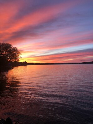 A sunset over a calm body of water with a silhouette of trees on the left. - Heavenly Lakeside Retreat (East Jordan)