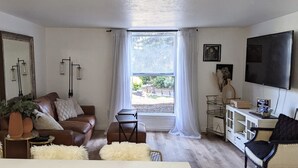 Un ampio soggiorno con una grande finestra, un divano, un tavolino, una TV e un mobile.