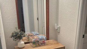 Un comò di legno con uno specchio sopra, un vaso con una pianta e un organizer di plastica con diversi oggetti sopra.
