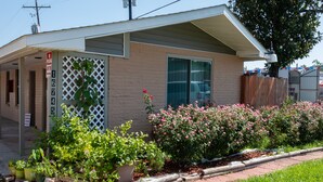 A single-story building with a garage door, a small porch, and a brick exterior. There are potted plants and flowers in front of the building. - Studio, 1 King Bed, Kitchenette - Non-Smoking (Baton Rouge)