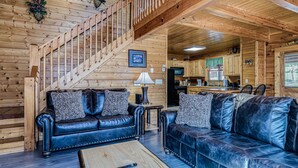 A wooden interior with a staircase, two leather sofas, a coffee table, and a kitchen area.