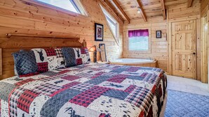A wooden cabin bedroom with a large bed, a skylight, a window with curtains, and a wooden door.