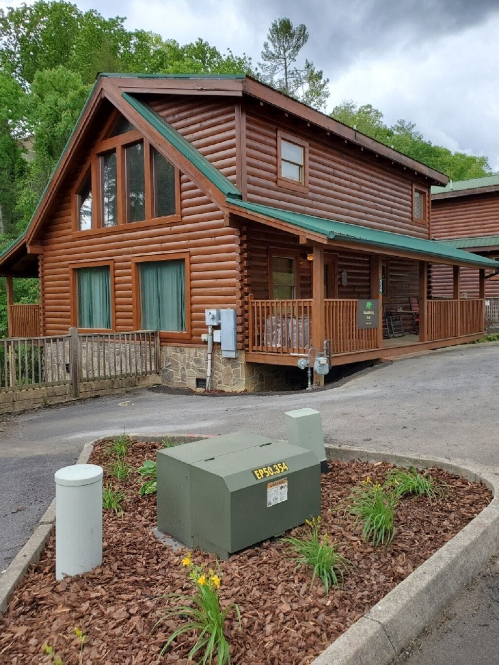A log cabin-style building with a porch, a stone foundation, and a green roof.