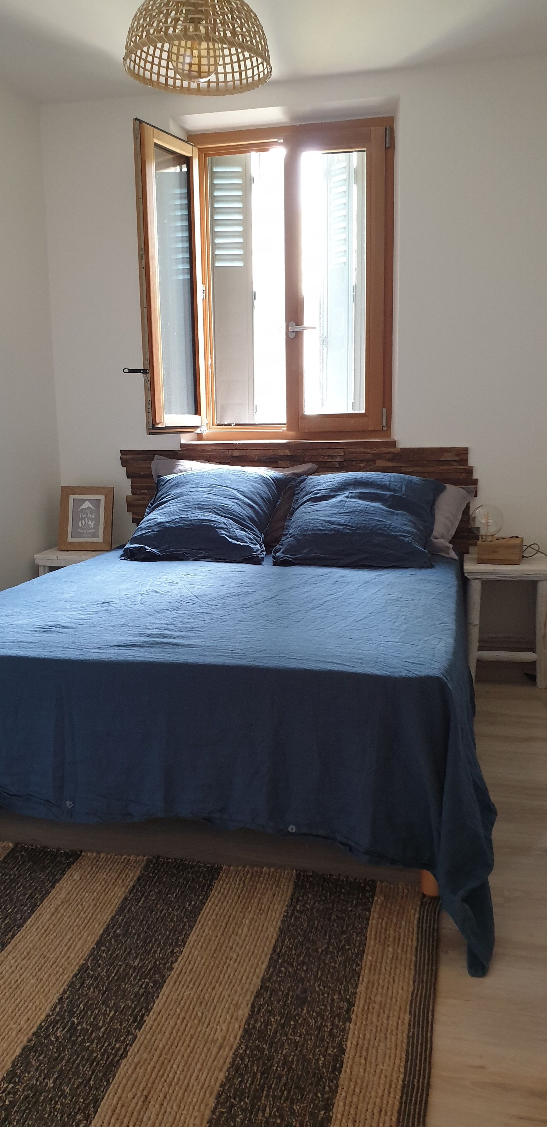 A bedroom with a bed, a window, a bedside table, and a rug.