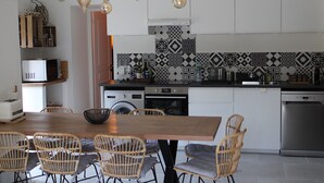 A modern kitchen with white cabinets, a wooden dining table, wicker chairs, and a patterned backsplash. - Village house, sleeps 8.  (Saint-Chaffrey)