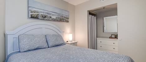 A bedroom with a bed, a nightstand, a bedside lamp, a dresser, a mirror, and a painting on the wall.