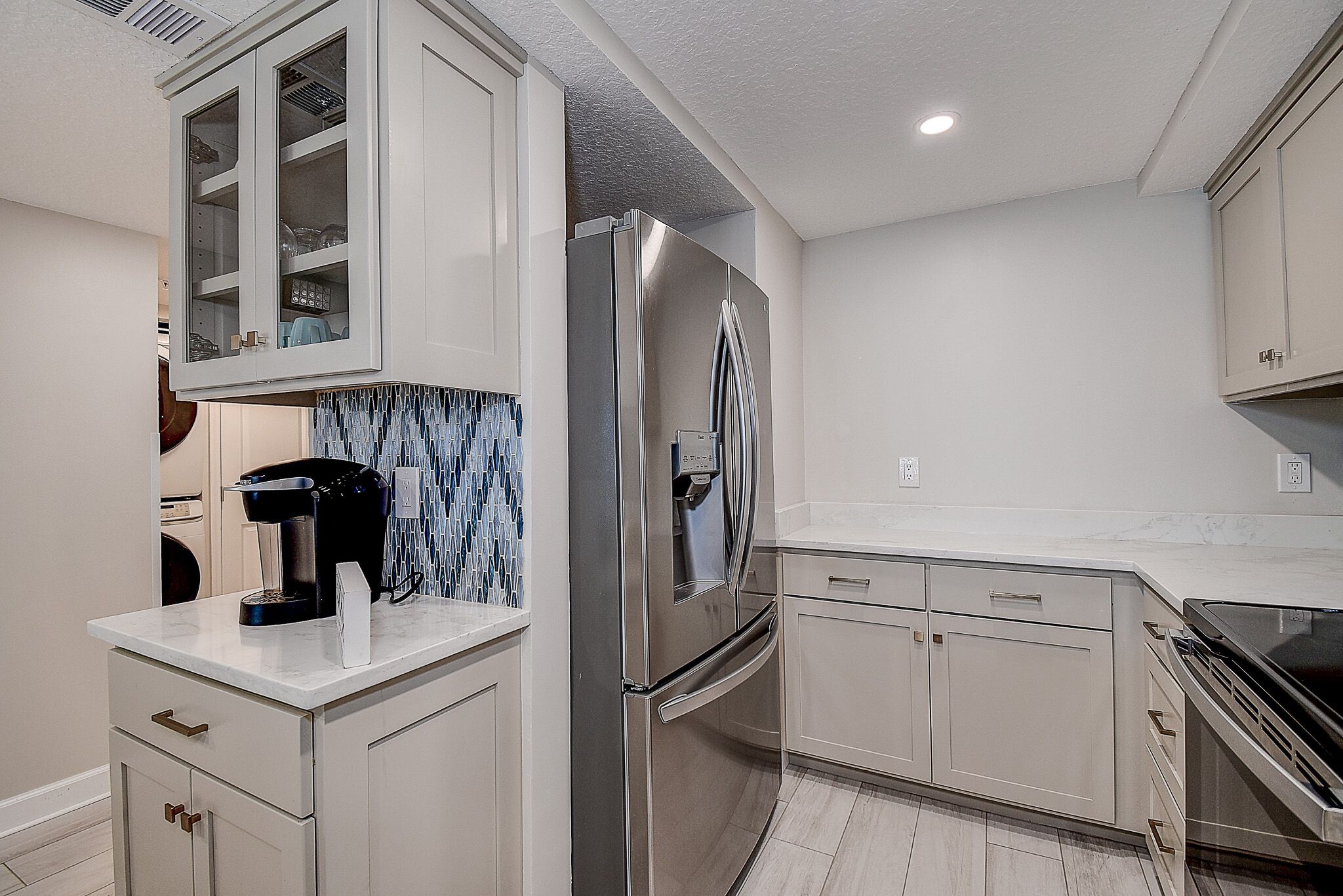 Una cocina moderna con refrigerador de acero inoxidable, armarios blancos y una cafetera en la encimera.