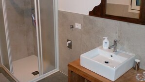 A bathroom with a glass-enclosed shower, a white sink with a wooden countertop, and a mirror above the sink. - Tourist House San SIsto (Sandrigo)
