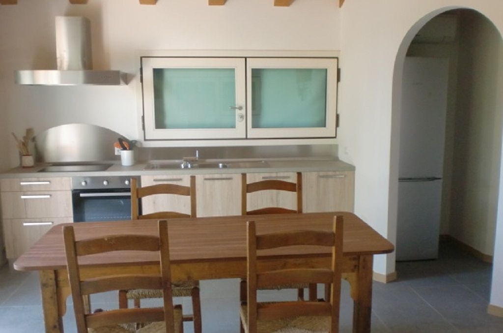 A kitchen with a wooden table and chairs, a stove, and cabinets.