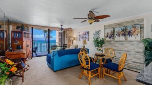 A living room with a blue sofa, wicker chairs, a dining table, and a ceiling fan. - Check out our Summer Discounts and Fantastic Views! (Lahaina)