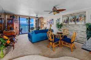 A living room with a blue sofa, wicker chairs, a dining table, and a ceiling fan.