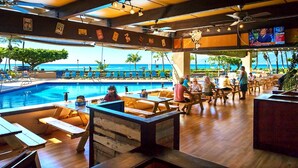 A poolside bar area with wooden tables and chairs, overlooking a pool and the ocean. - Check out our Summer Discounts and Fantastic Views! (Lahaina)