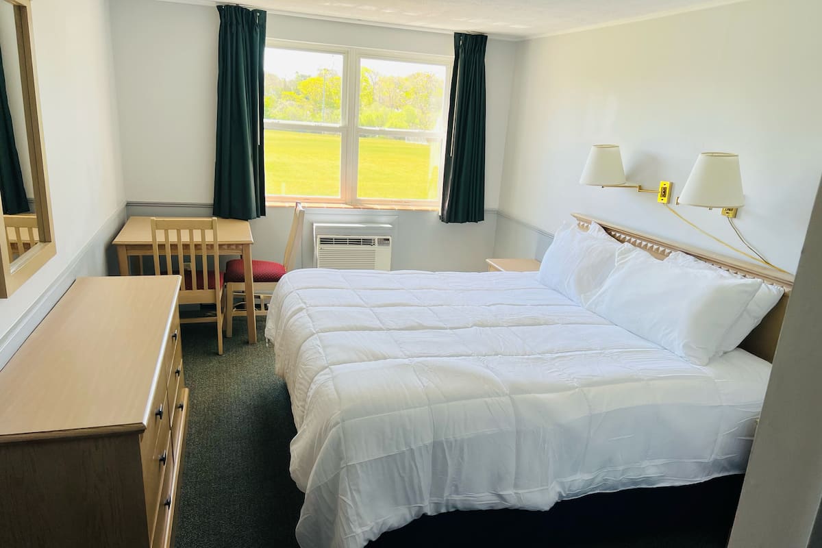 A hotel room with a large bed, a desk, a chair, and a window with curtains.