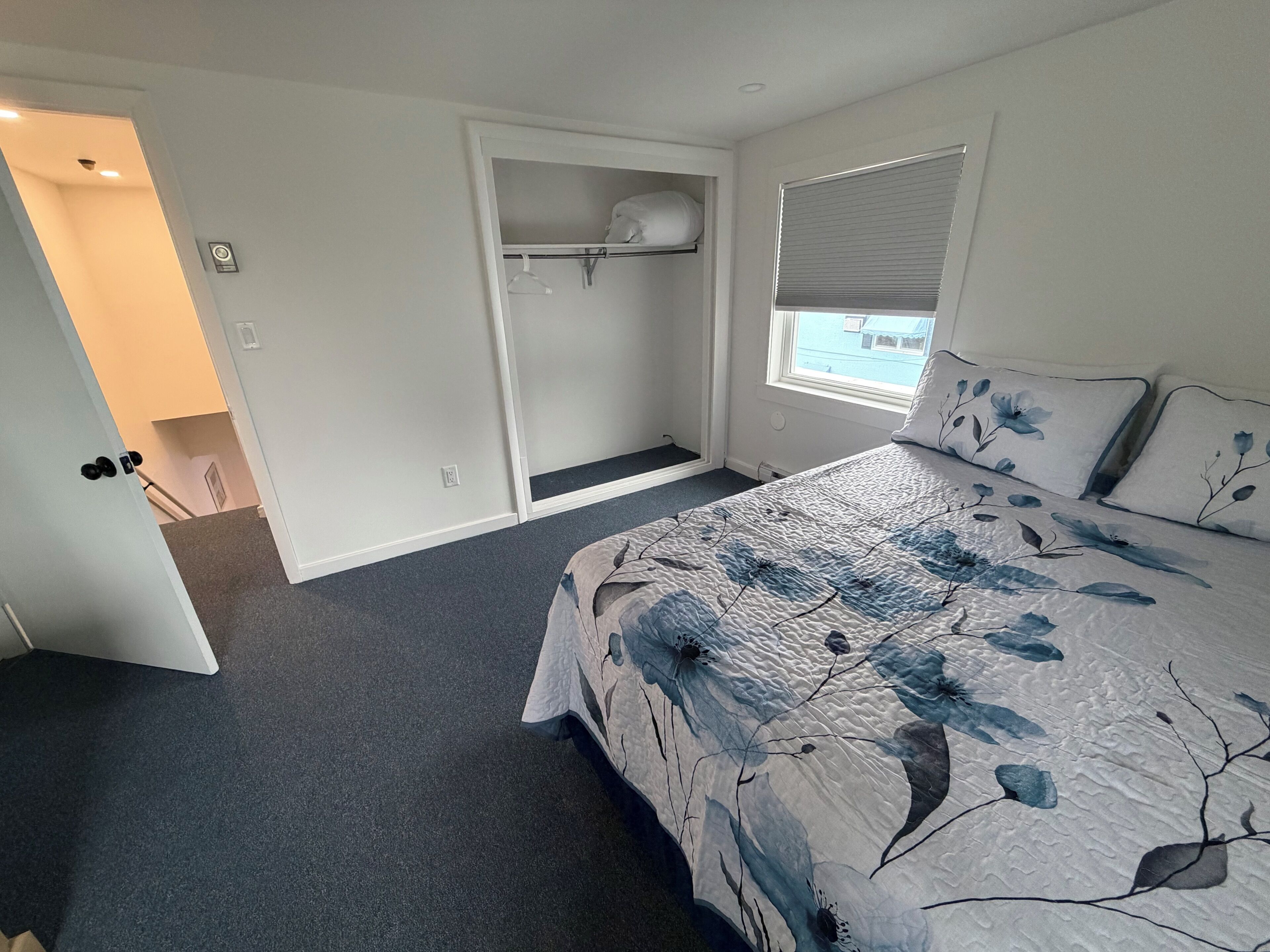Une chambre à coucher comprenant un lit, une armoire, une fenêtre avec des stores et une porte donnant sur une autre pièce.