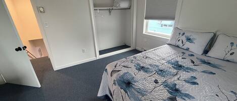 Une chambre à coucher comprenant un lit, une armoire, une fenêtre avec des stores et une porte donnant sur une autre pièce.