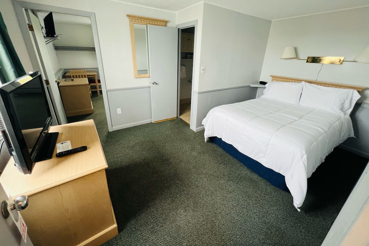 A hotel room with a bed, a desk with a computer, a mirror, and a television.