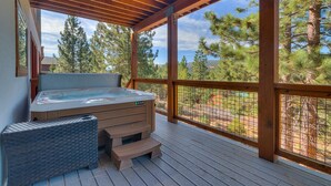 A hot tub on a wooden deck with a view of pine trees.