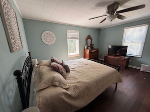 Een slaapkamer met een bed, een dressoir, een televisie en decoratieve wandobjecten.