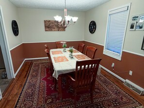 A dining room with a table set for four, surrounded by wooden chairs, a patterned rug, and a chandelier.