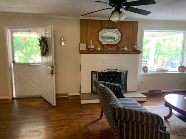 A living room with a sofa, a fireplace, a ceiling fan, and a door leading to an outdoor area.
